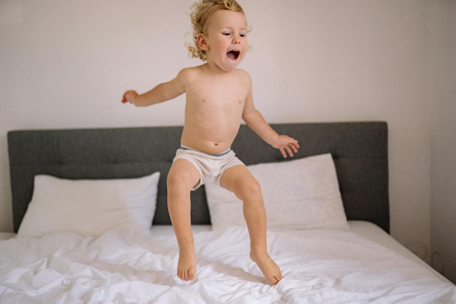 Child joyfully jumping on a bed in a bright room, capturing playful energy and fun.